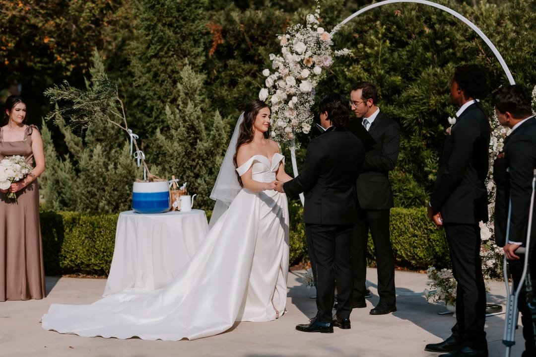 Bride facing the groom and officiant at the round arch, her train spread across the terrace