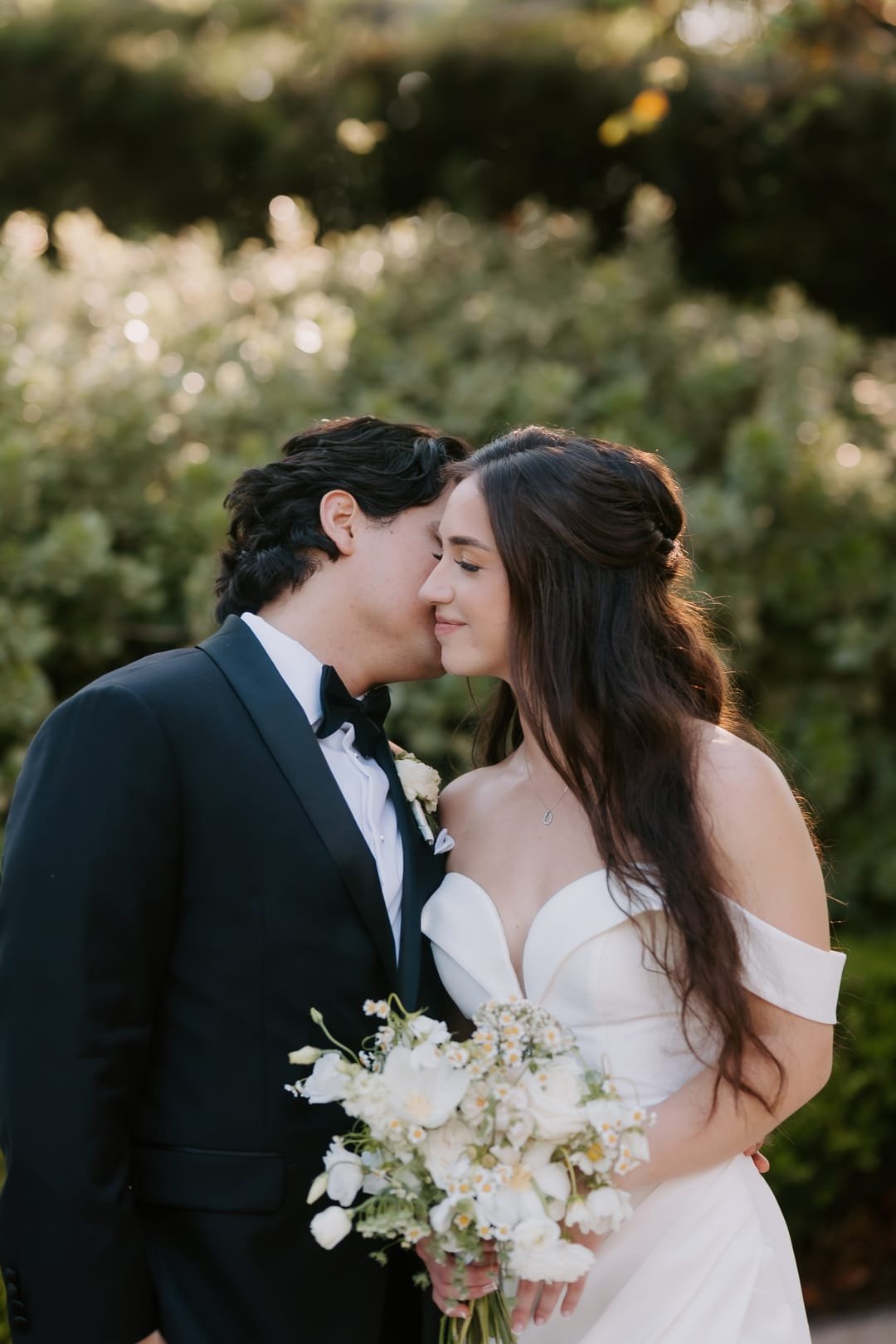 Groom leaning in forehead to forehead with the bride, her bouquet held between them