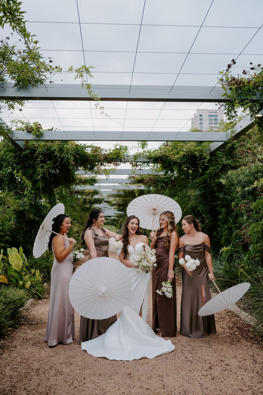Bridal party holding paper parasols under a vine-covered pergola