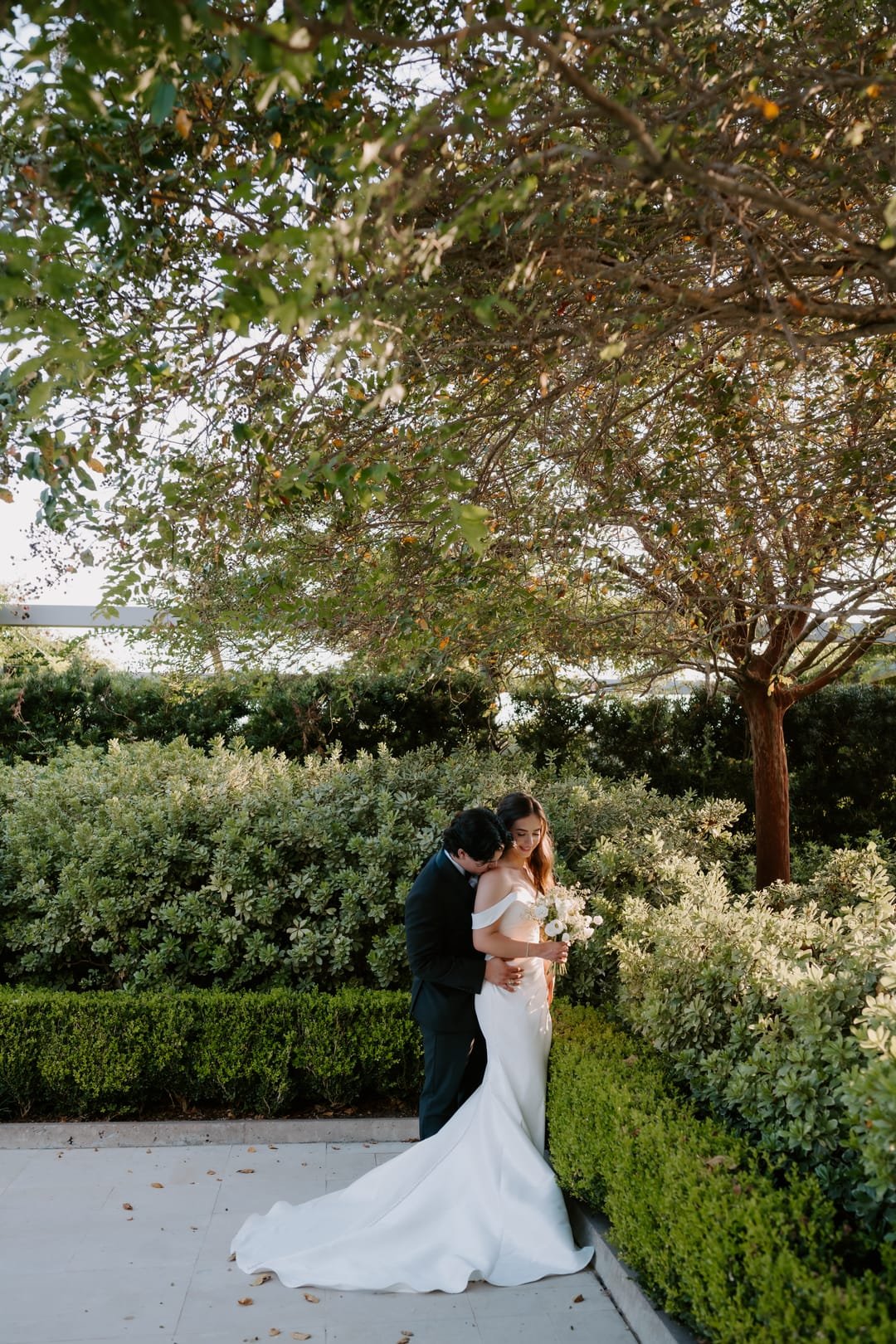 Couple embracing on a garden path beneath a broad flowering tree