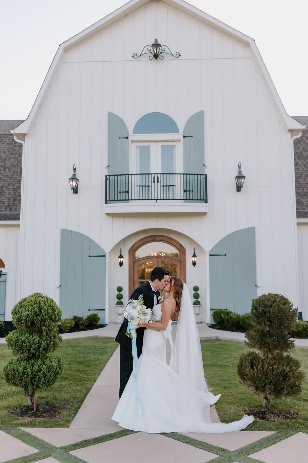 Couple kissing under the barn archway, her train fanned out across the lawn