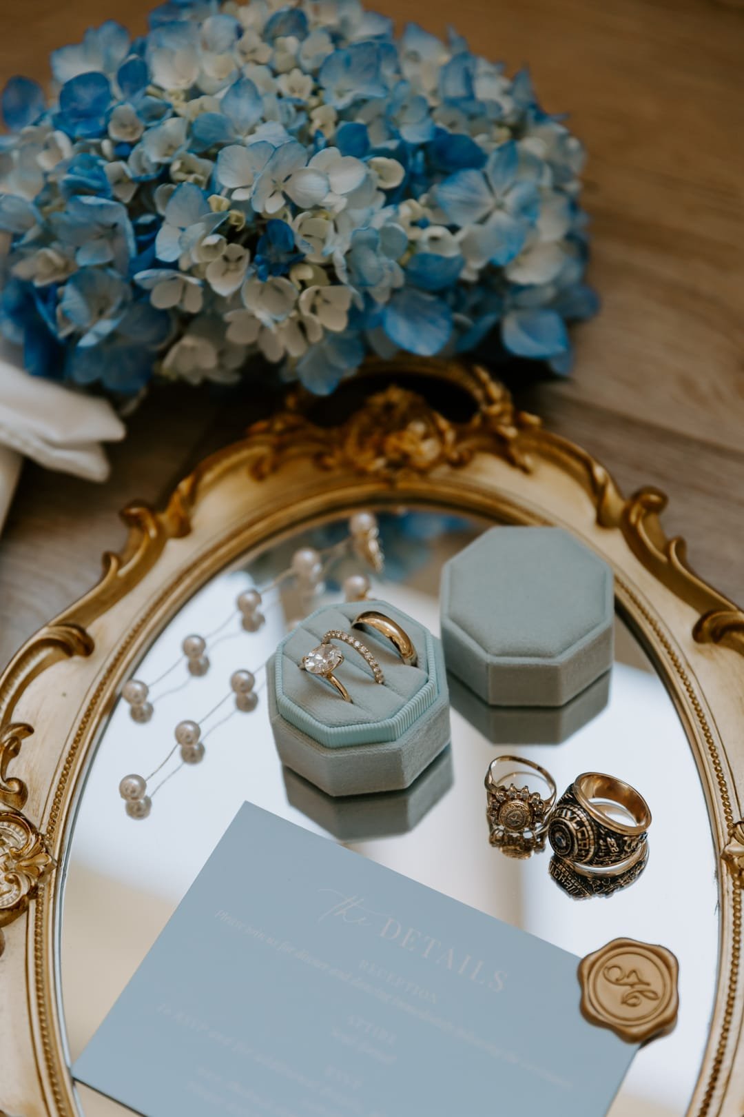 Rings in a dusty-blue box on a gilded mirror tray, pearl earrings and blue hydrangea alongside