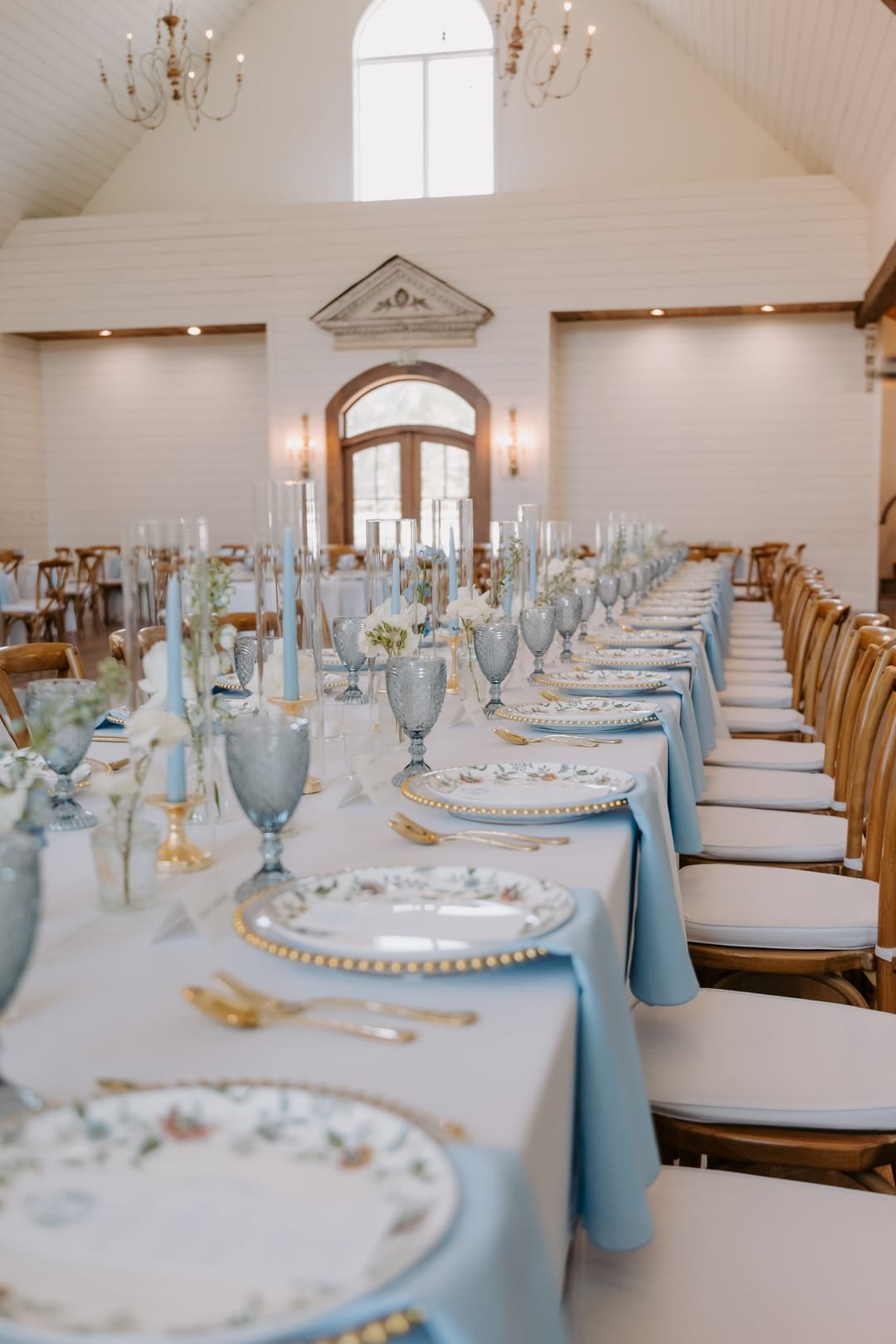 Long reception table laid in pale blue and gold beneath a vaulted white ceiling
