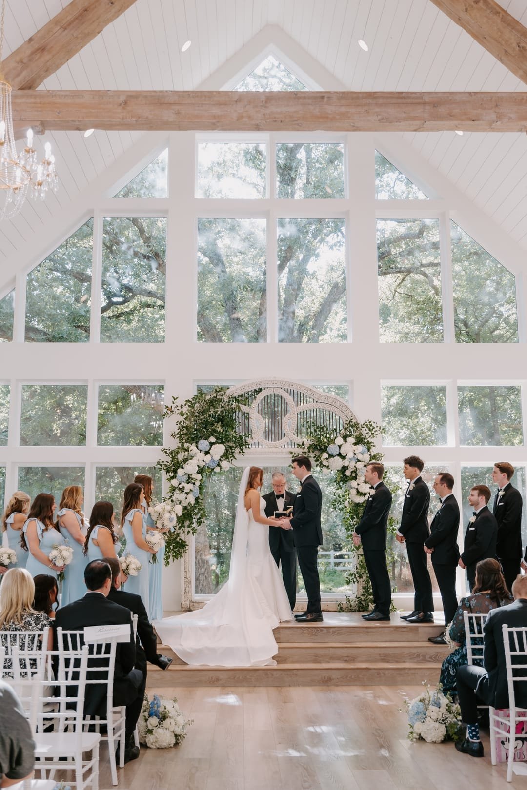 Chapel ceremony framed by a wall of arched windows and the oak canopy beyond