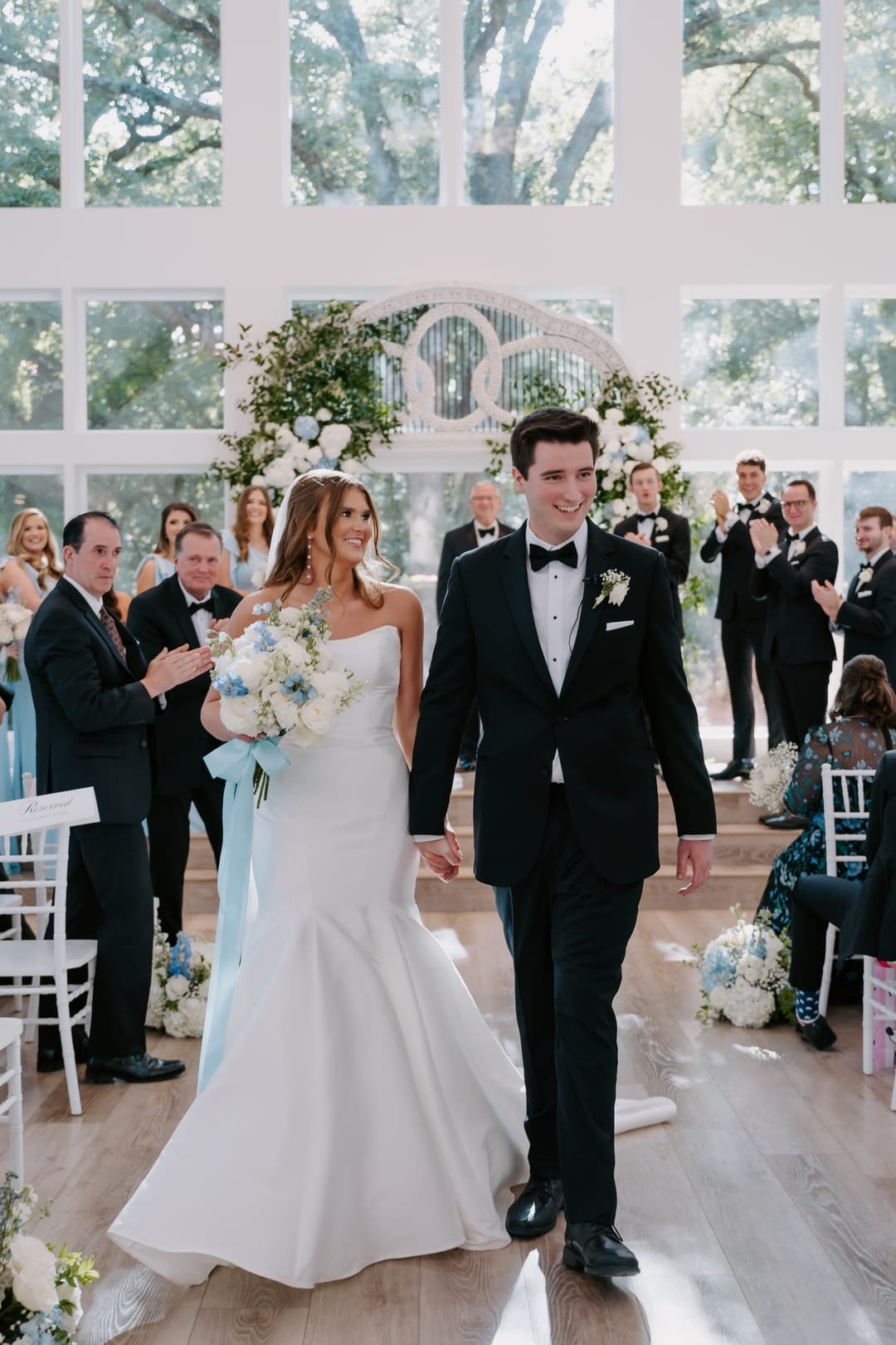 Newlyweds walking back up the aisle hand in hand as guests applaud