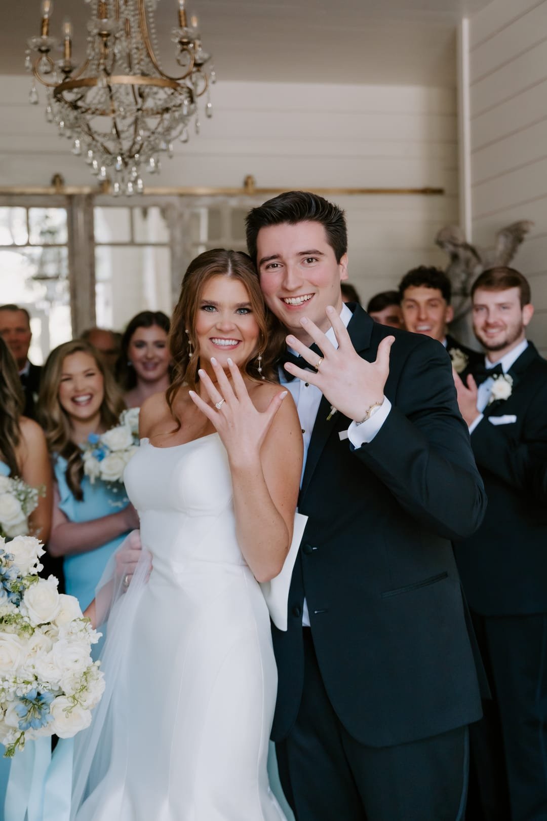 Bride and groom holding their ringed hands up to the camera, both laughing