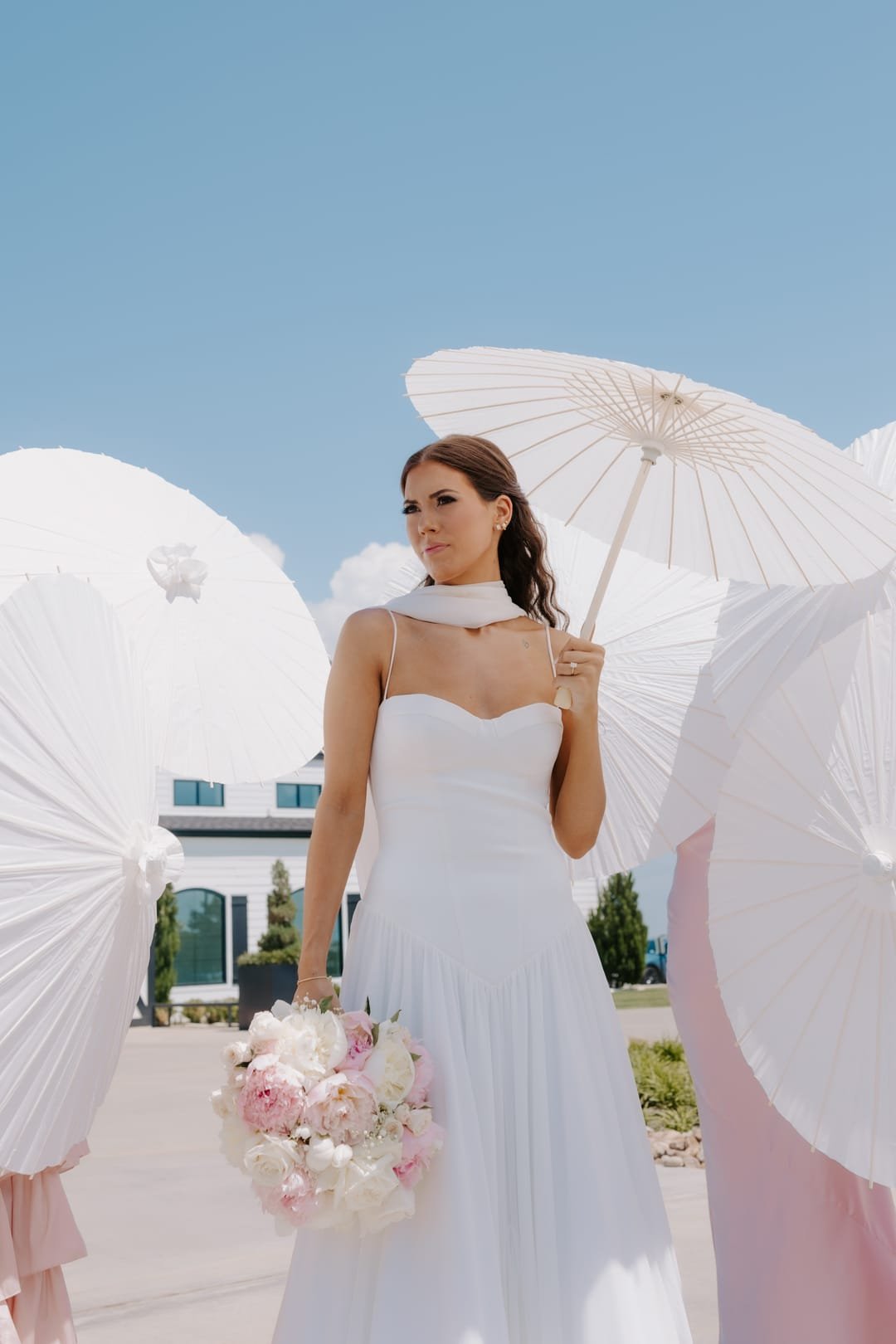 Bride holding a paper parasol and a blush bouquet against a clear blue sky