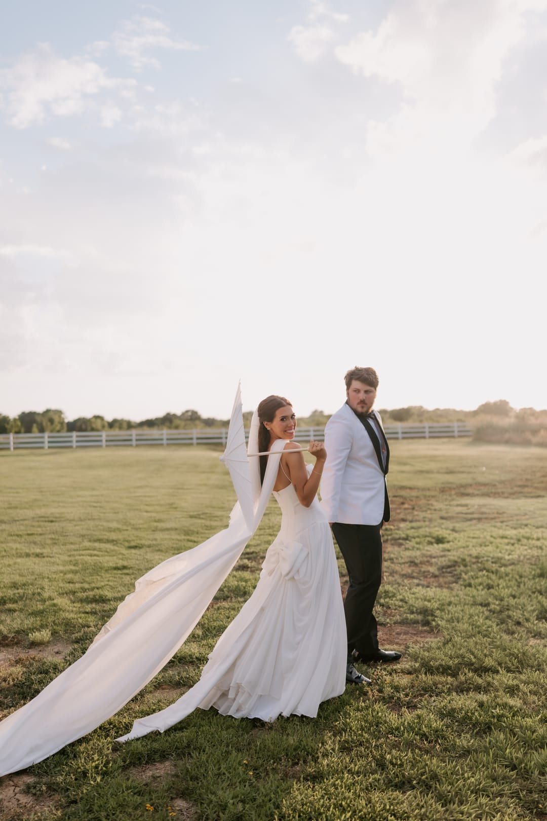 Bride's veil lifting on the wind as the couple stand together in the open field