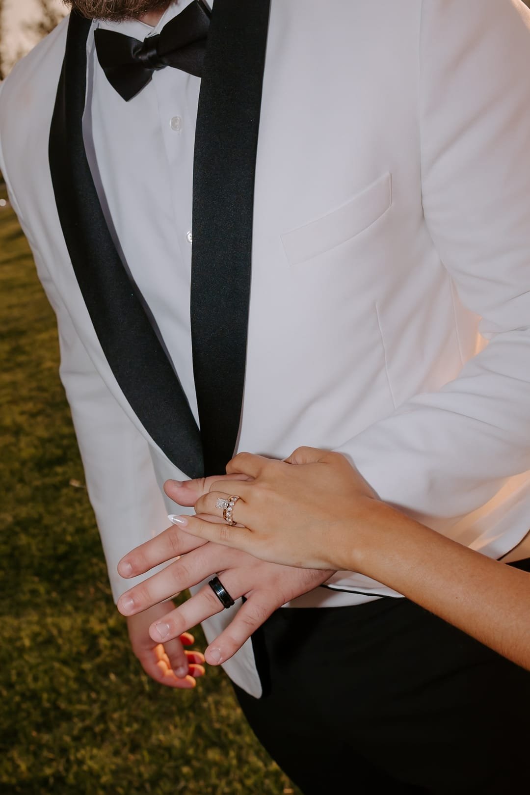 Close view of joined hands and both wedding bands against a white dinner jacket