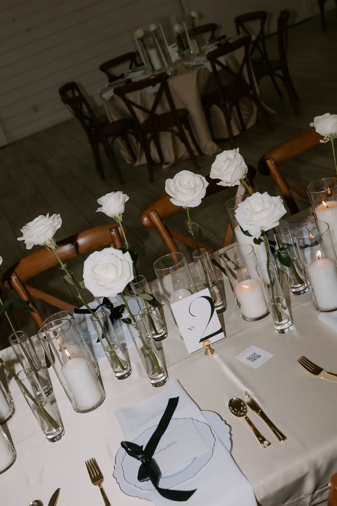 Reception table lined with single white roses in glass vases, candles and gold flatware